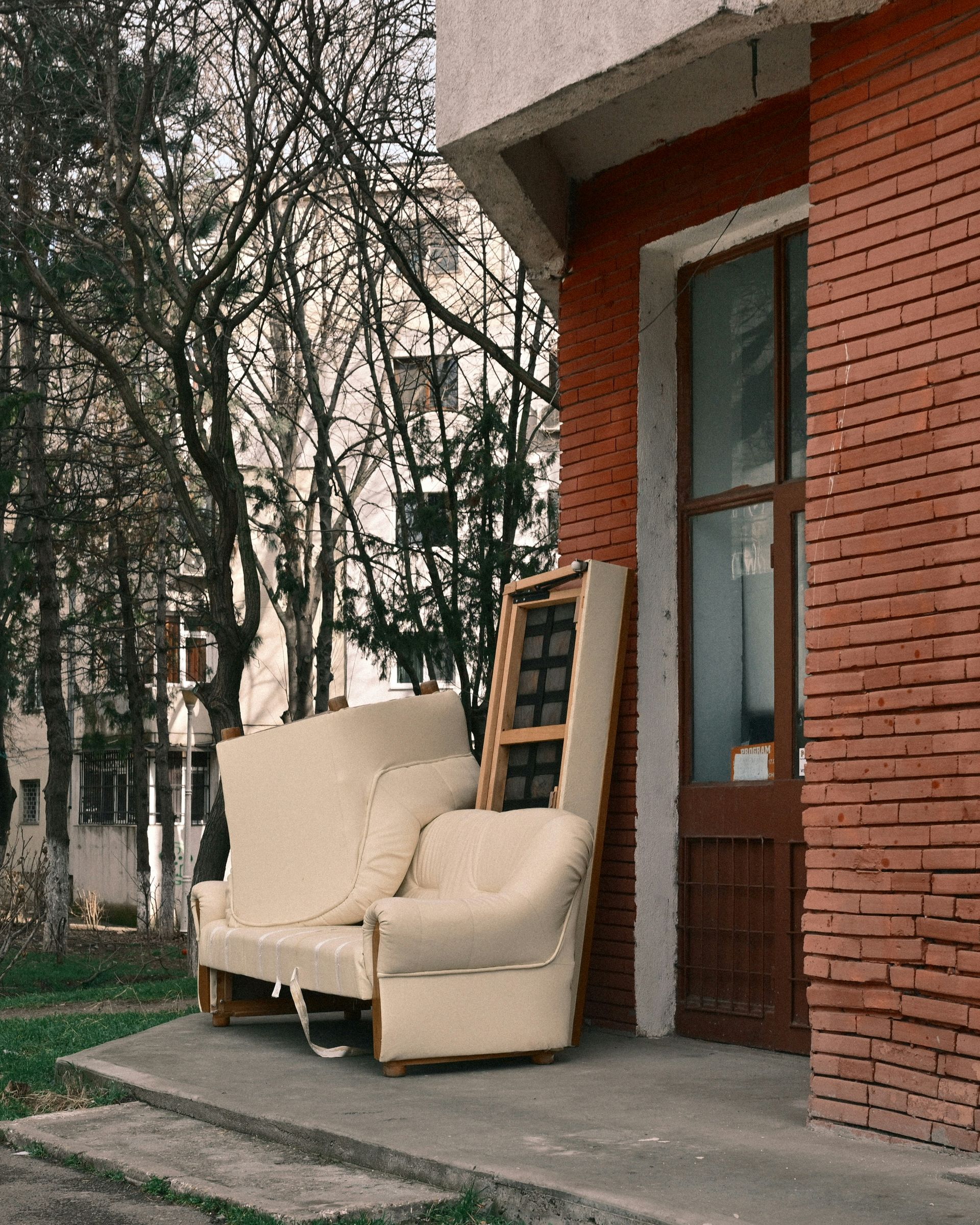 An old armchair and sofa left outside a brick building